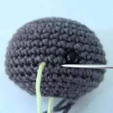 Needle with lime yarn embroidering the blush beside the eye of the crochet bat head