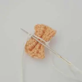 Needle threading yarn through the middle of the crochet bow tie