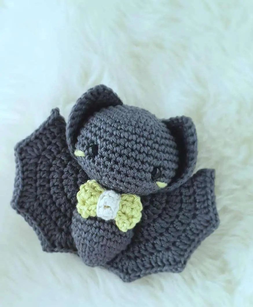 Gray crochet baby bat amigurumi with a lime green bow tie and folded wings