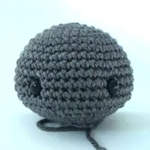 Gray crochet bat head with black safety eyes, stuffed and rounded