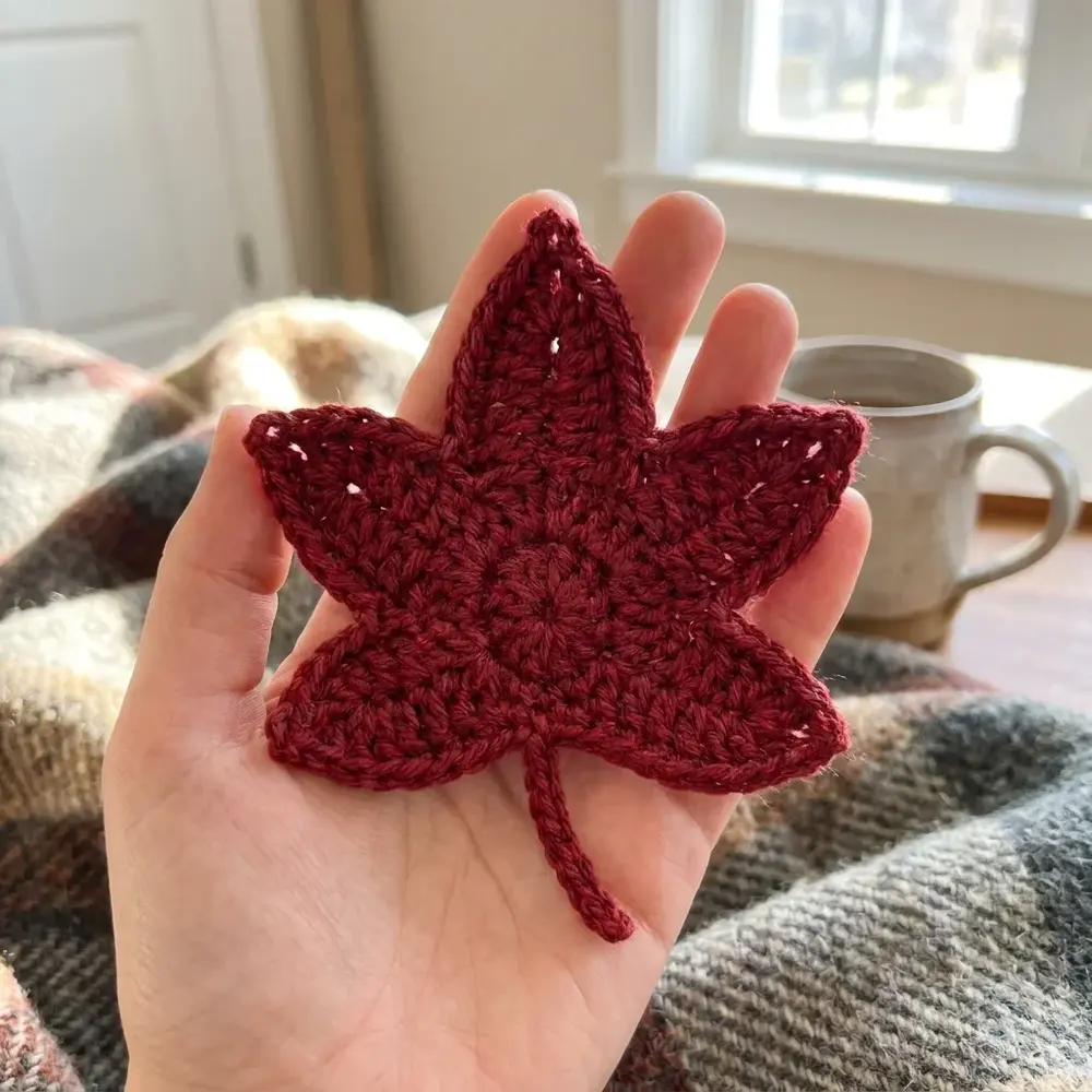 Red crochet maple leaf with five lobes and a stem held in an open hand