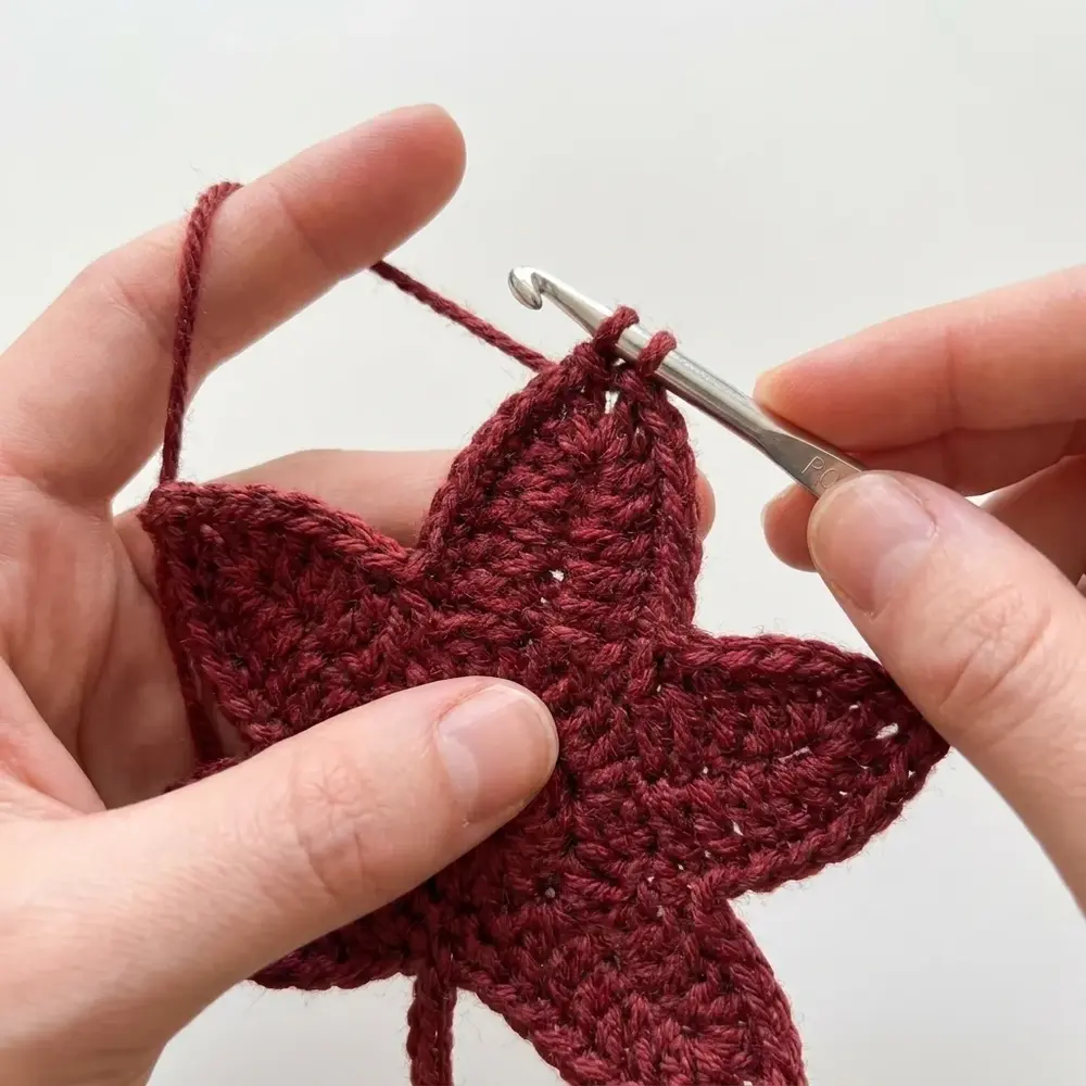 Working a pointed lobe of a red crochet maple leaf with a silver crochet hook