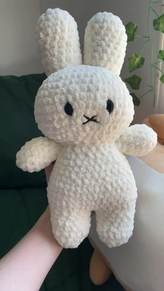 A cream-colored crochet bunny with long ears held in a hand