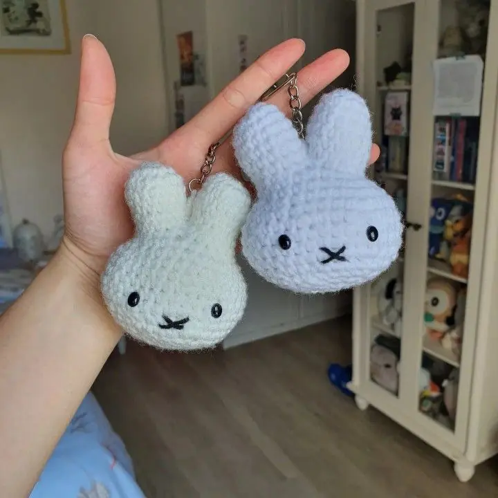 Two small crochet bunny-head keychains, one white and one light blue, held in a hand