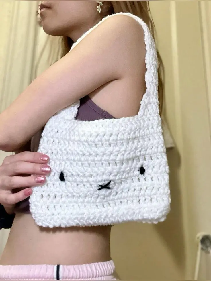 A white crochet shoulder bag with a bunny face on the front
