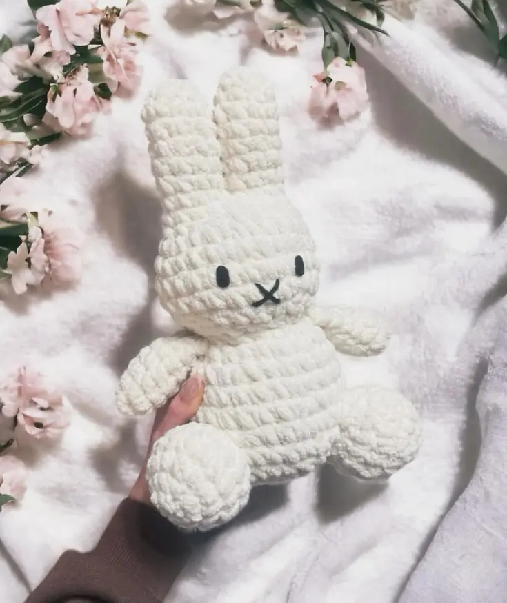 A white crochet bunny lying among pink blossoms
