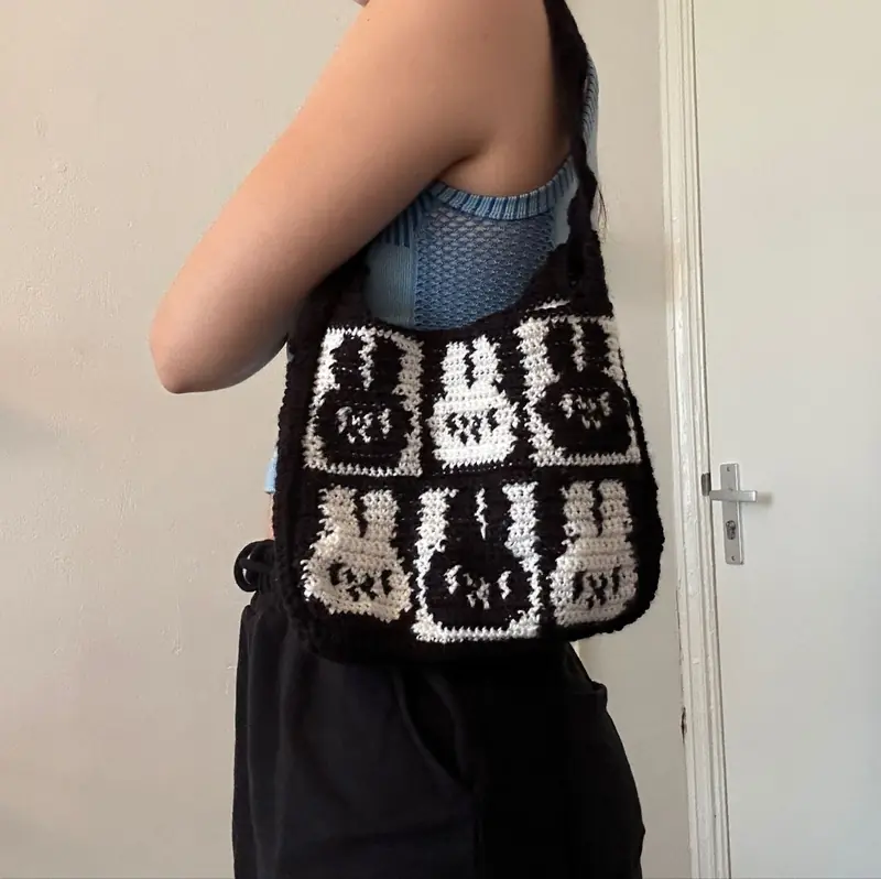 A black-and-white crochet shoulder bag made of granny squares with bunny faces