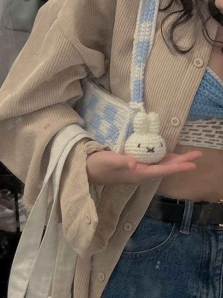 A small crochet bunny charm hanging from a blue checkered bag strap