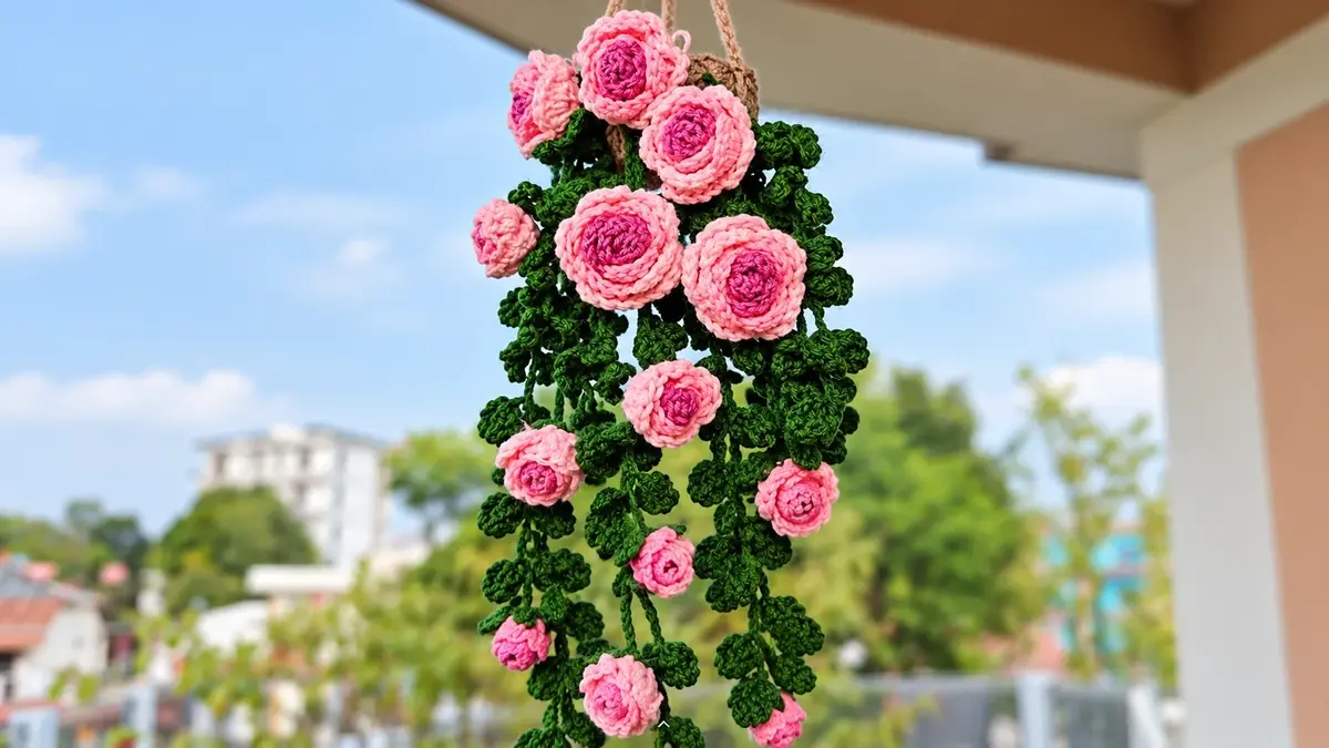 Crochet hanging rose vine with light pink roses, dark pink centers and green leaves hanging outdoors