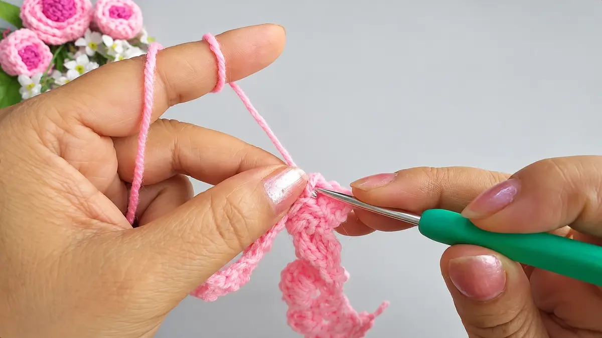 Working pink crochet rows with a green crochet hook for a rose flower