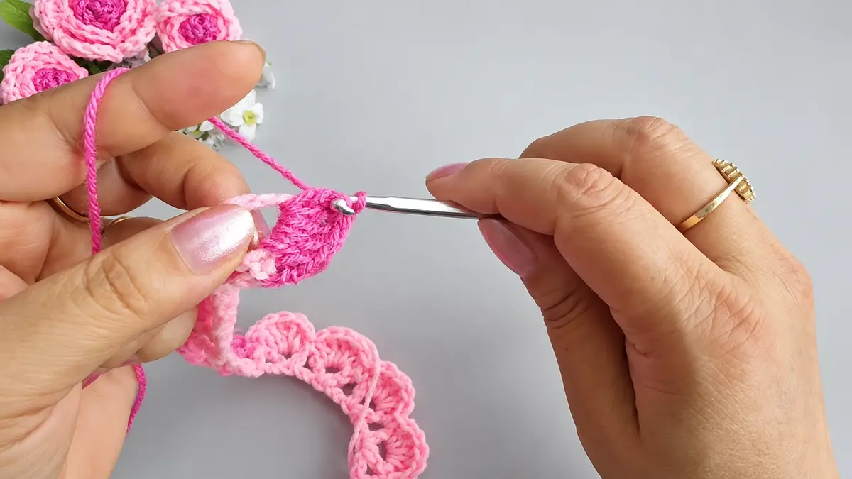 Crocheting a pink ruffled strip that will be rolled into a rose